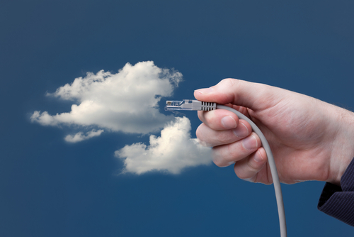 a hand holding an ethernet cable as if to plug it in to clouds on blue background