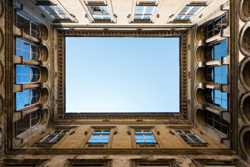 Photograph taken from the courtyard of an old building open to the sky showing the architectural detail and many windows to demonstrate the concept of virtualization whereby one physical structure houses many smaller ones.