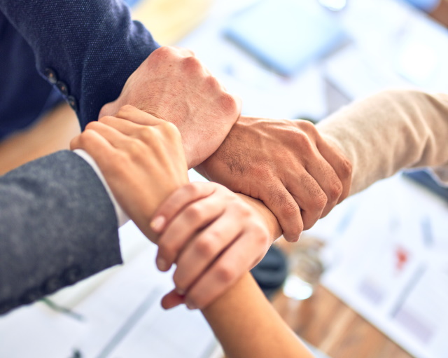 Four hands both male and female each gripping the wrist of the person to their left to form a square signifying a wider array of services